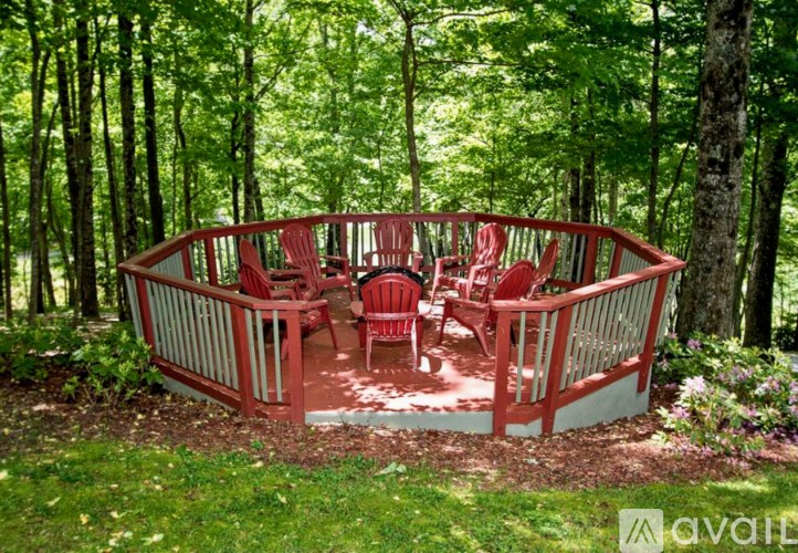 A red wooden table and chairs are set up on a deck in the woods.
