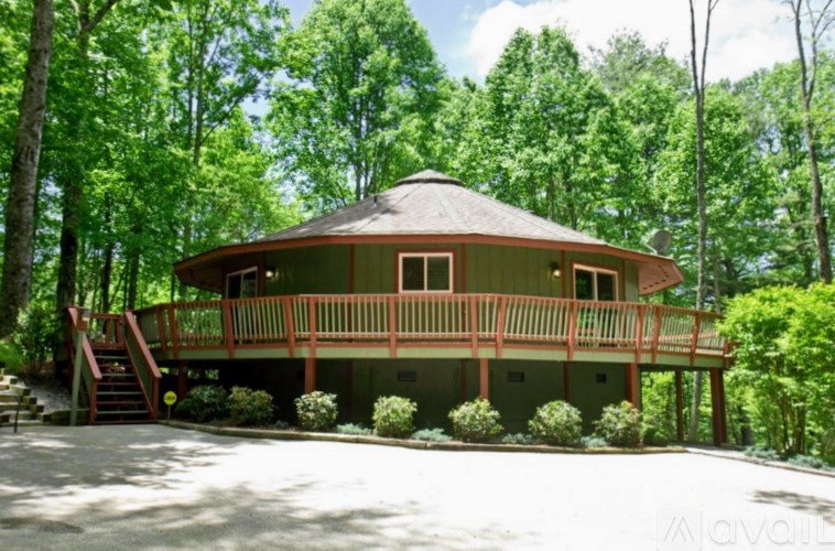 A round house with a porch is surrounded by green trees.