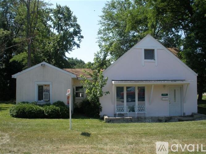 A white house with a porch and a sign in front.