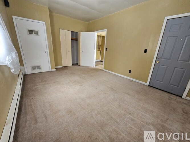 A room with beige walls and carpeted floor with a white door and a grey door.