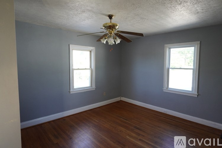 A room with a ceiling fan and two windows.