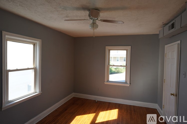 A room with a ceiling fan and two windows.