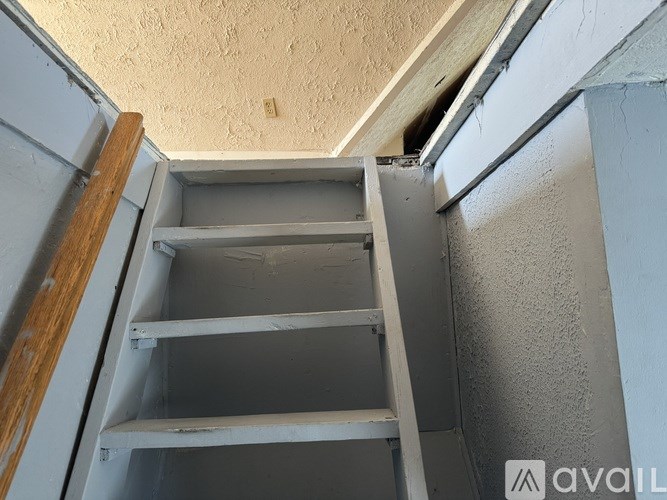 A white shelving unit with three shelves is open, revealing a wooden floor.