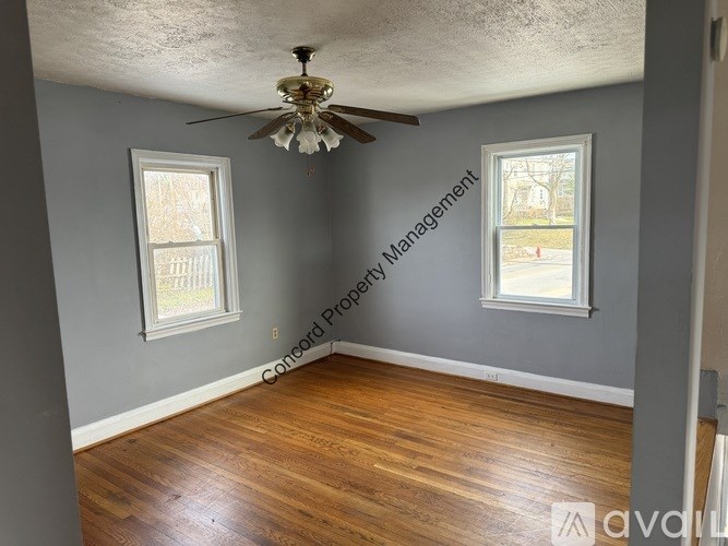 A room with a ceiling fan and two windows.