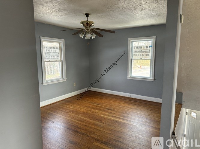 A room with a ceiling fan and two windows.