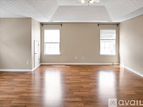 A spacious room with wooden floors and two windows.