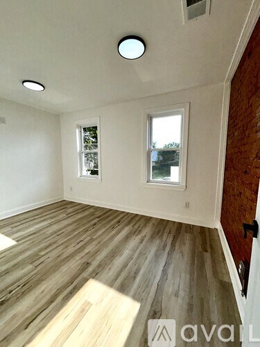 A room with wooden flooring and two windows.