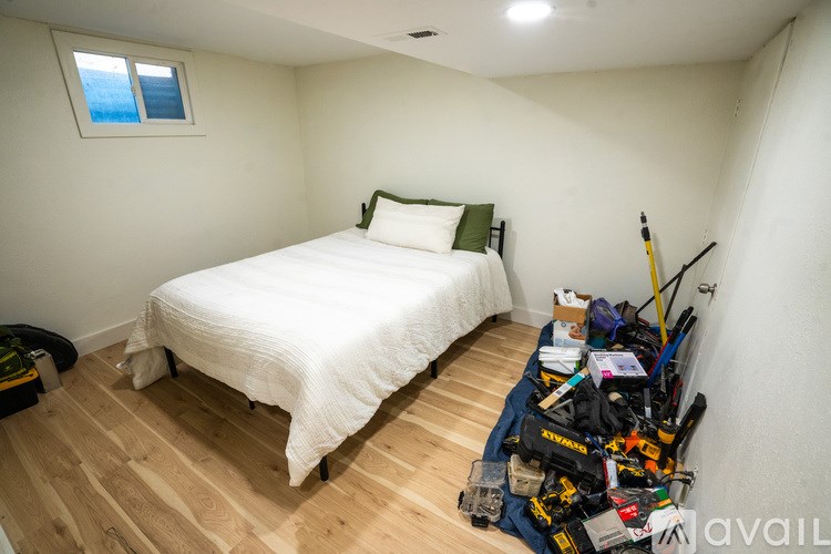 A bedroom with a bed, a window, and a pile of items on the floor.