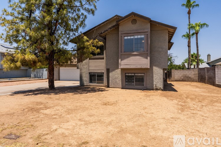 A house with a brown roof and tan walls is surrounded by a fence and has a tree in front of it.