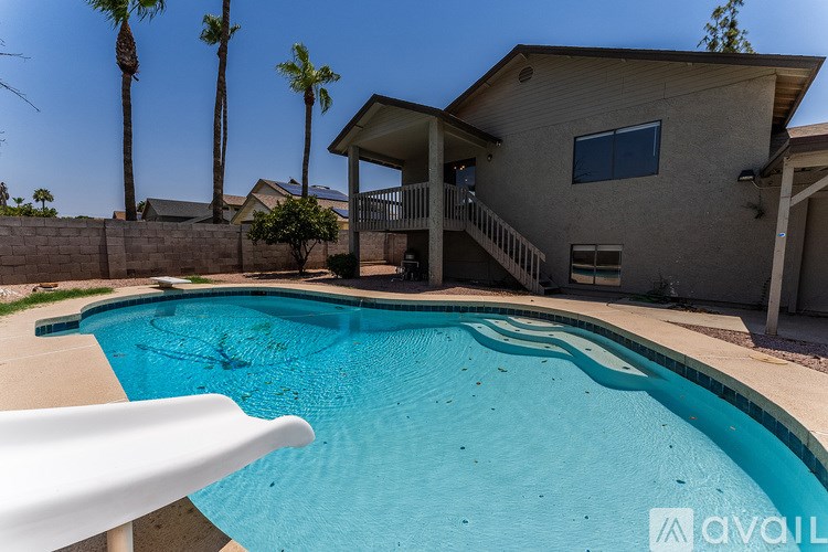 A pool in a backyard with a house and palm trees in the background.