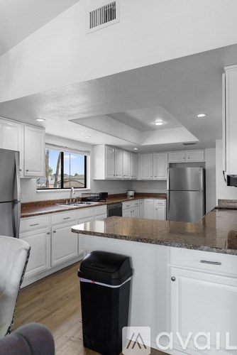 A modern kitchen with white cabinets and a black trash bin.