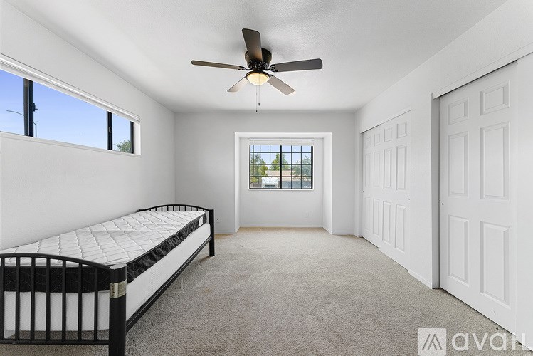 A bedroom with a bed, a ceiling fan, and a window with a view.