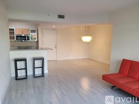 A living room with a red couch and a kitchen area in the background.
