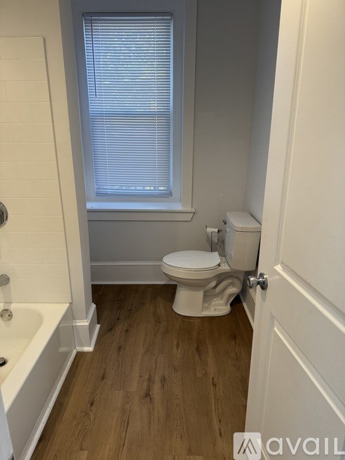 A white toilet in a small bathroom with wooden floors and a window.