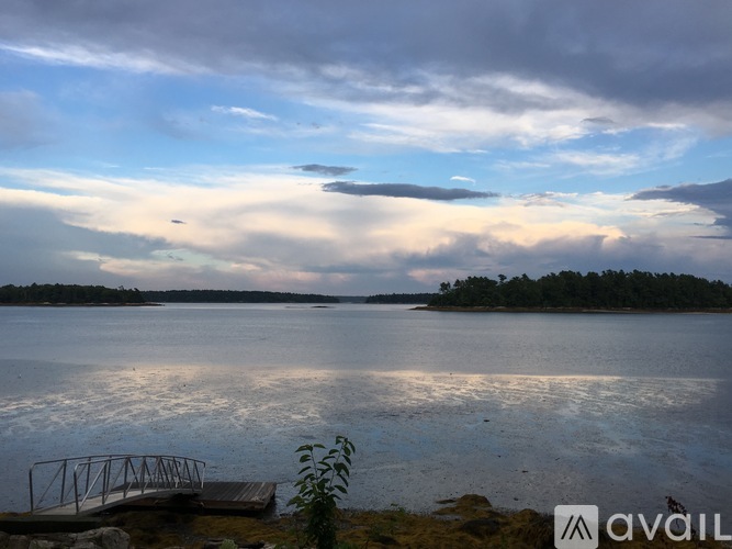 A calm lake with a dock and trees in the distance under a cloudy sky.