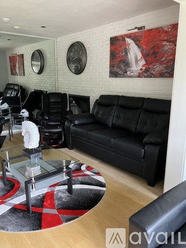 A living room with black leather furniture and a red and black rug.