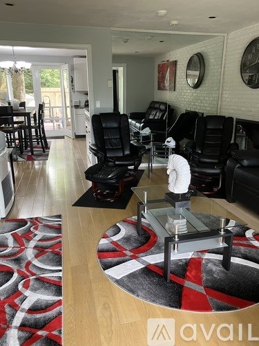 A man is standing in a living room with black leather chairs and a red and black rug.