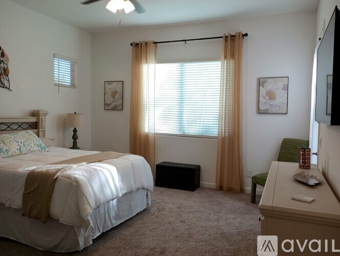 A bedroom with a bed, desk, and window with curtains.