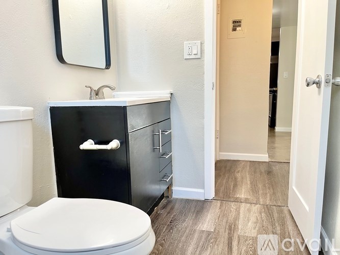 A bathroom with a white toilet, a sink with a black cabinet and a mirror above it.