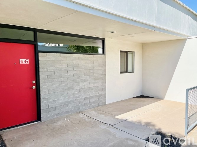 A red door with the number 16 on it is on the left side of a white wall.