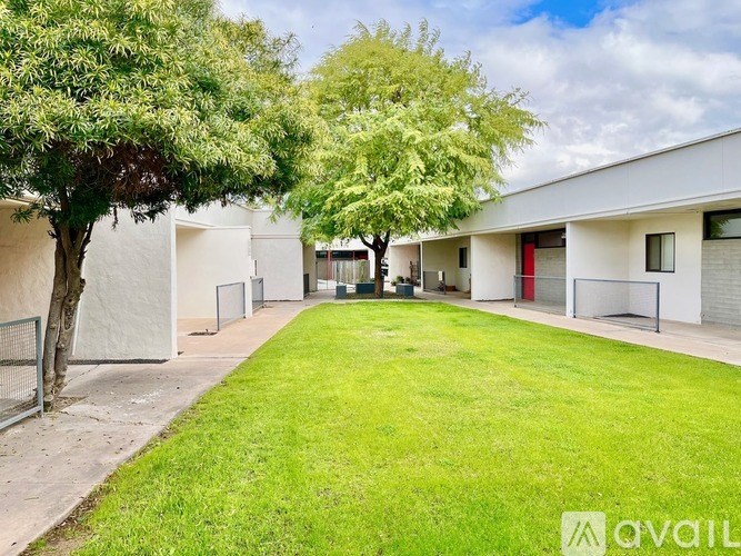 A grassy area in front of a white building with trees on the left.