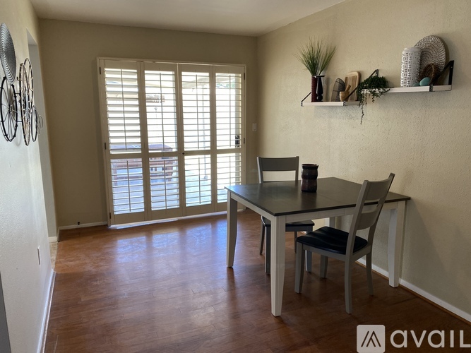 A dining room with a table and chairs and a wall shelf with plants and decorations.