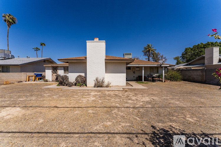 A house with a white chimney is surrounded by a gravel driveway and palm trees.