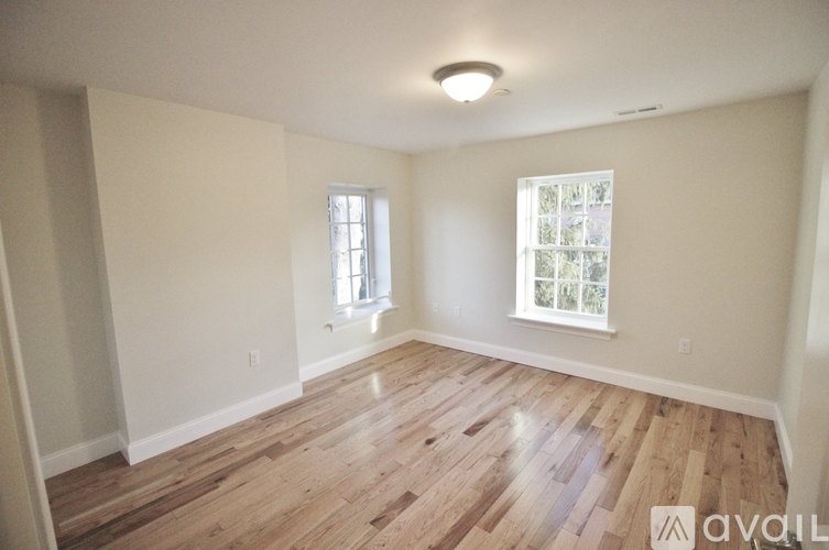 A spacious room with wooden floors and two windows.