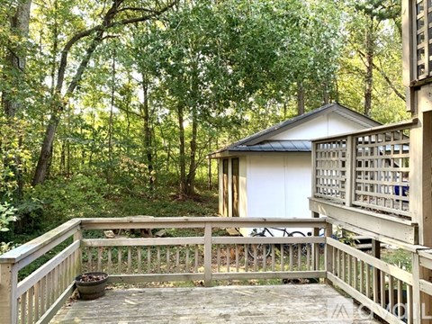 A small building with a gabled roof is surrounded by a wooden deck and a forest.