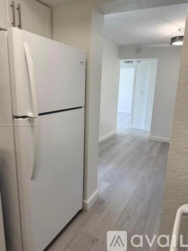 A white fridge in a room with wooden flooring.