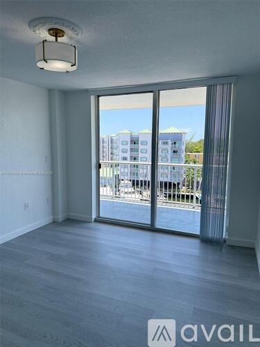 A room with a sliding glass door leading to a balcony with a view of a building.