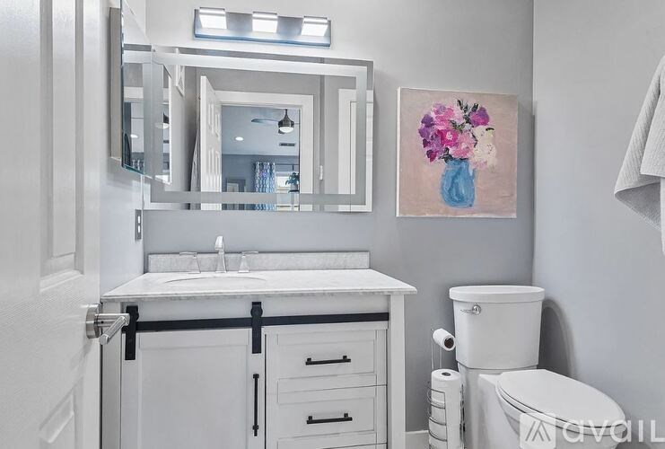 A bathroom with a white toilet, sink, and a painting of flowers.