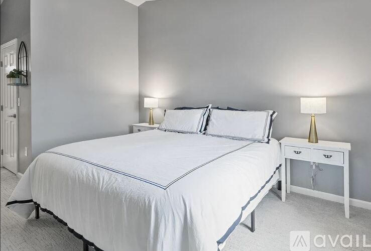 A bedroom with a white bed and a white nightstand with a lamp.