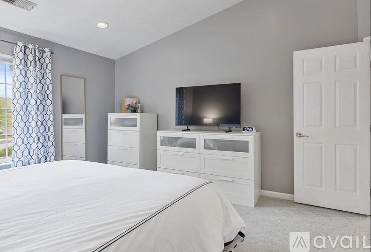 A bedroom with a large bed, a television, and a window with curtains.
