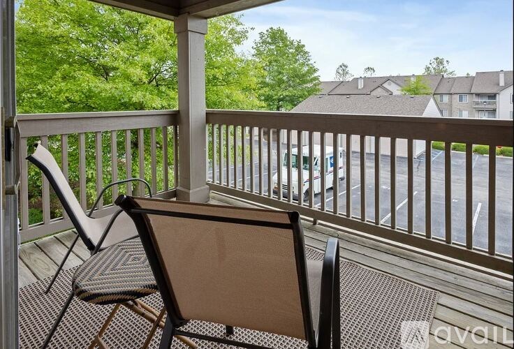 Two chairs are on a porch with a view of a parking lot and houses.