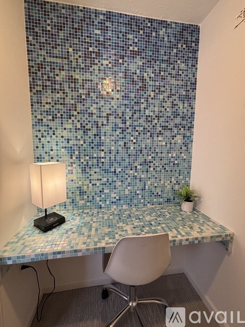 A blue tiled wall with a white chair and a table with a lamp on it.