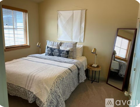 A bedroom with a large bed and a window with blinds.