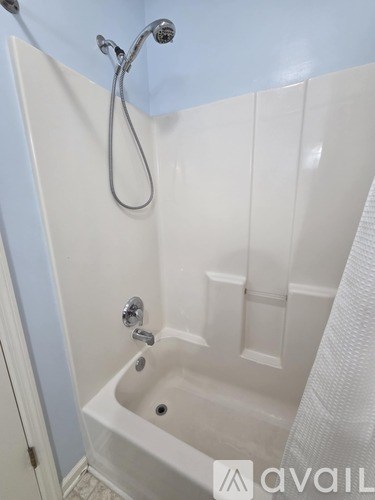 A white bathtub with a shower head and a white towel hanging on the side.