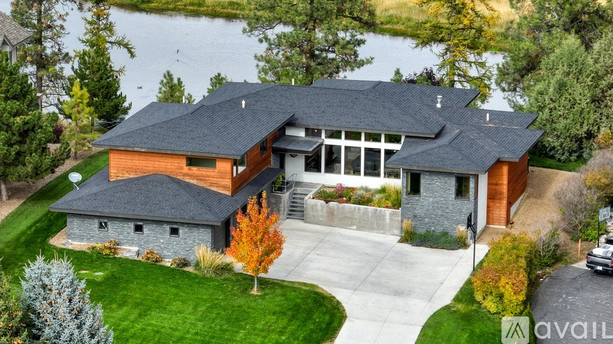 A modern house with a large front yard and a lake in the background.