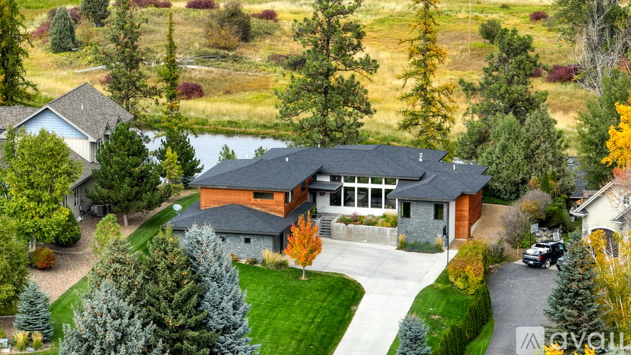 A large house with a grey roof and a stone wall is surrounded by trees.