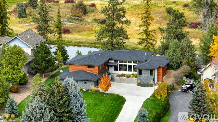 A large house with a grey roof and a stone wall is surrounded by trees.
