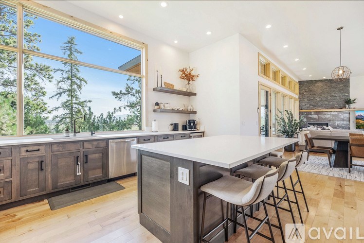 A modern kitchen with a large island and a view of the forest outside the window.