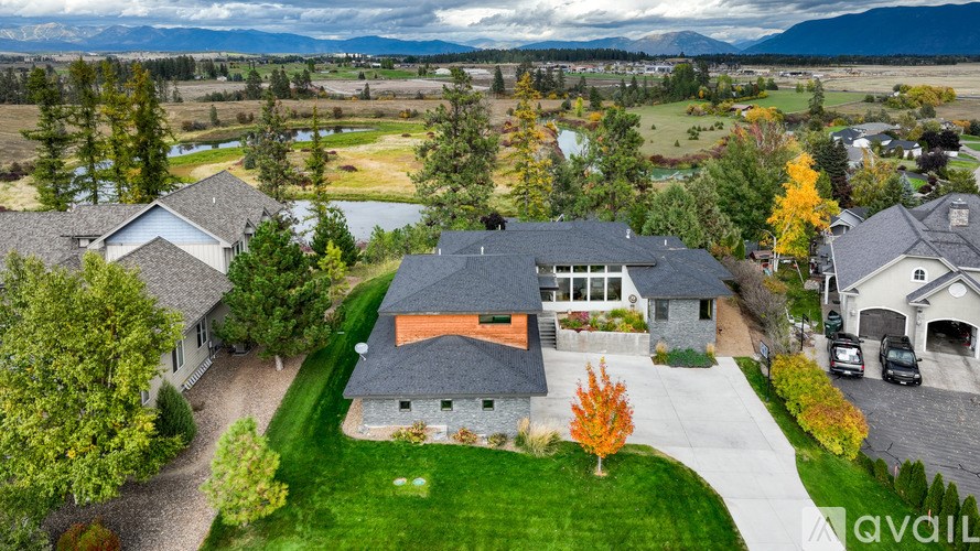 A house with a grey roof and a brown roof is surrounded by green grass and trees.