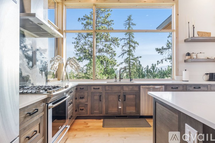 A modern kitchen with a large window overlooking a forest.