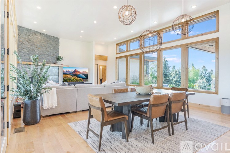 A modern dining room with a stone fireplace and a large window overlooking a forest.