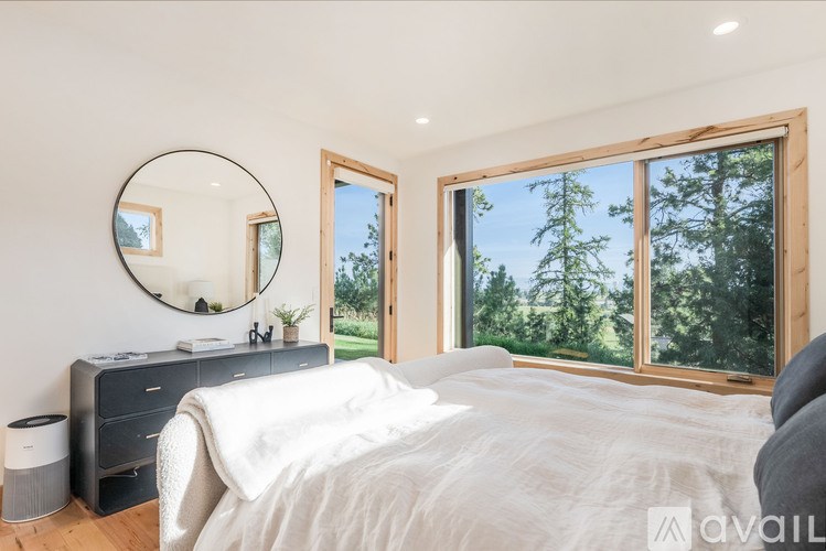 A bedroom with a large bed, a round mirror, and a window overlooking a forest.
