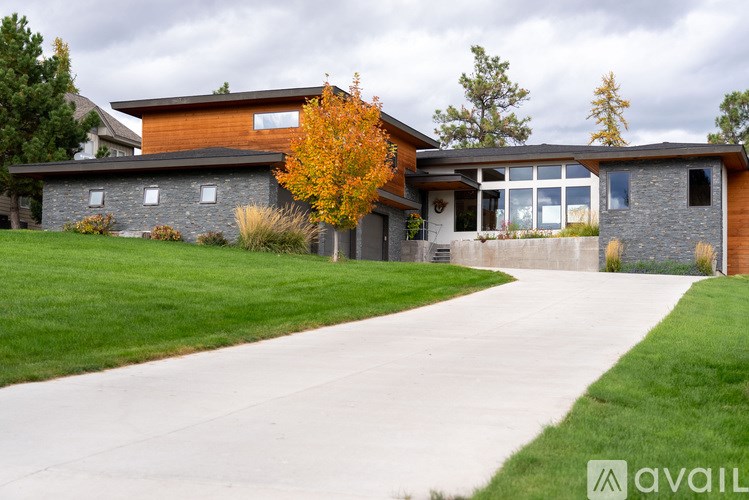 A modern house with a stone wall and a large front yard.
