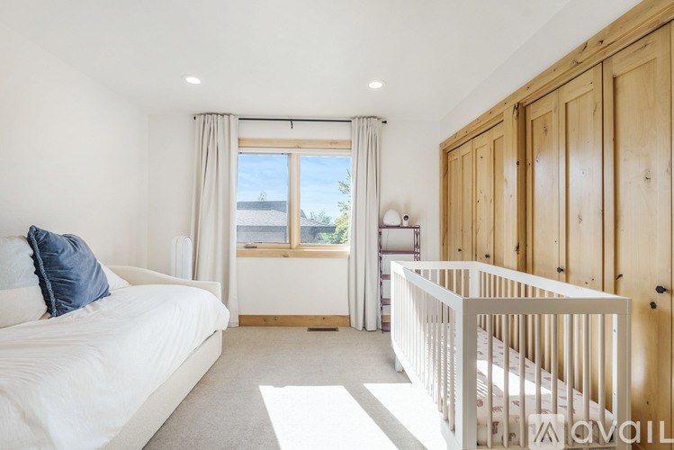 A white bedroom with a large window and a white crib.