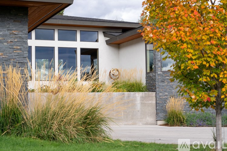 A modern house with a stone wall and a tree with orange leaves.