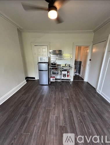 A kitchen with a black fridge, a microwave, and a metal rack with a pot on it.